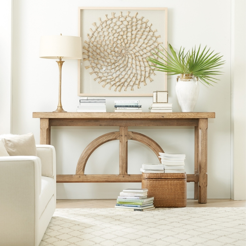 light brown wood modern console table with accessories and artwork next to white armchair