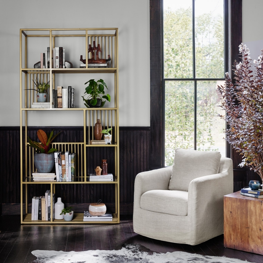 tall, gold, open bookcase next to white arm chair and wood square side table.