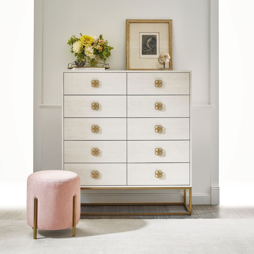 white dresser with gold handles and base behind small round pink ottoman