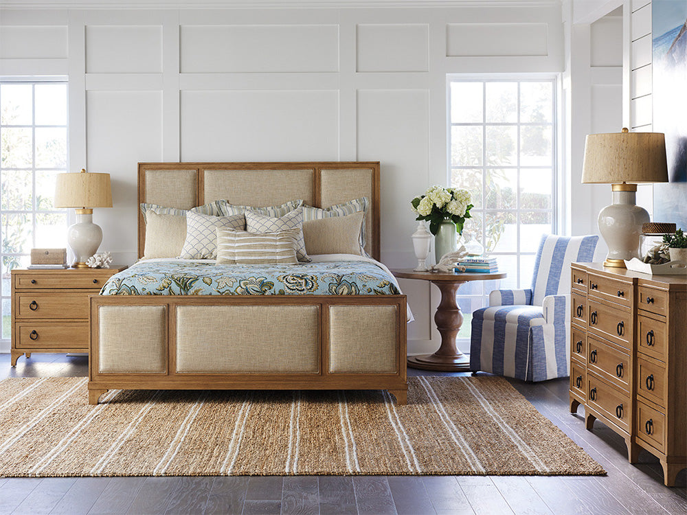 A coastal-style bedroom scene from Barclay Butera featuring a wood and fabric bed with matching nightstand and dresser.