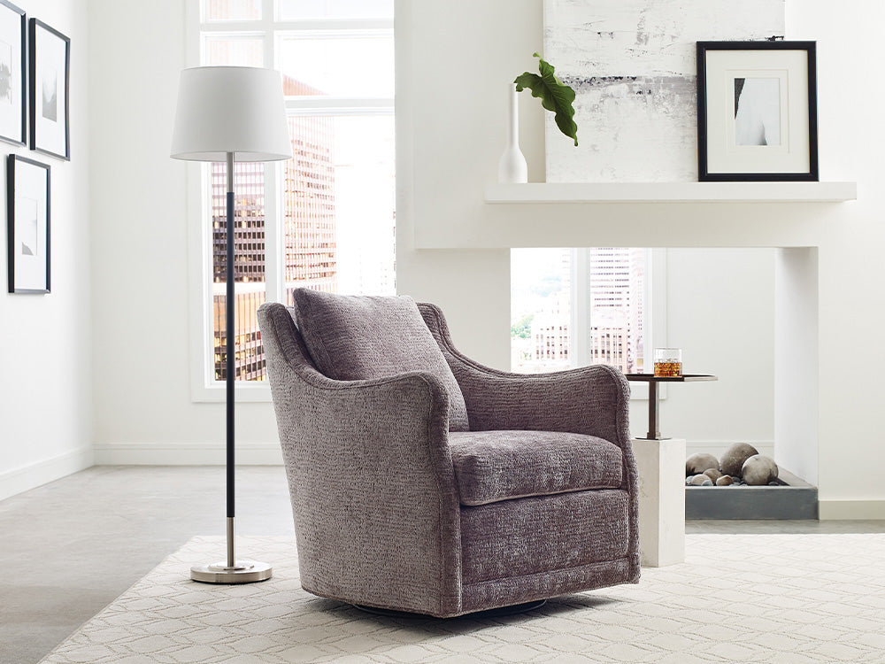 A purple-gray fabric swivel chair in a brightly-lit living room from Jessica Charles.