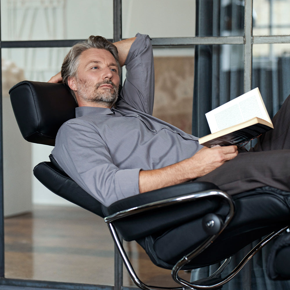 A person reclining while reading a book in a black leather chair