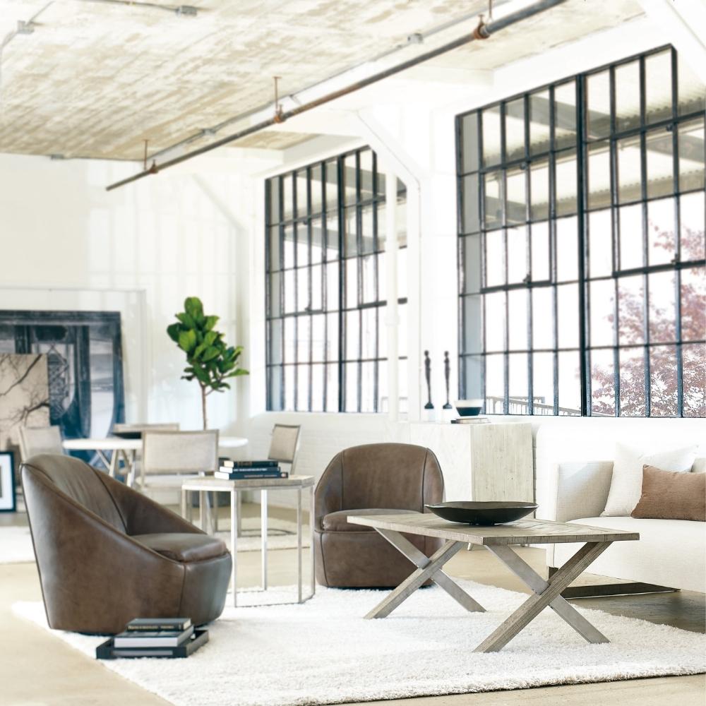 loft living room scene with two brown leather chairs, white sofa, and wood and metal coffee table. Dining area in background