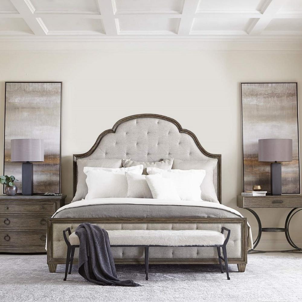 bedroom scene with large traditional wood and fabric tufted bed, nightstands on either side. Bench at foot of bed.