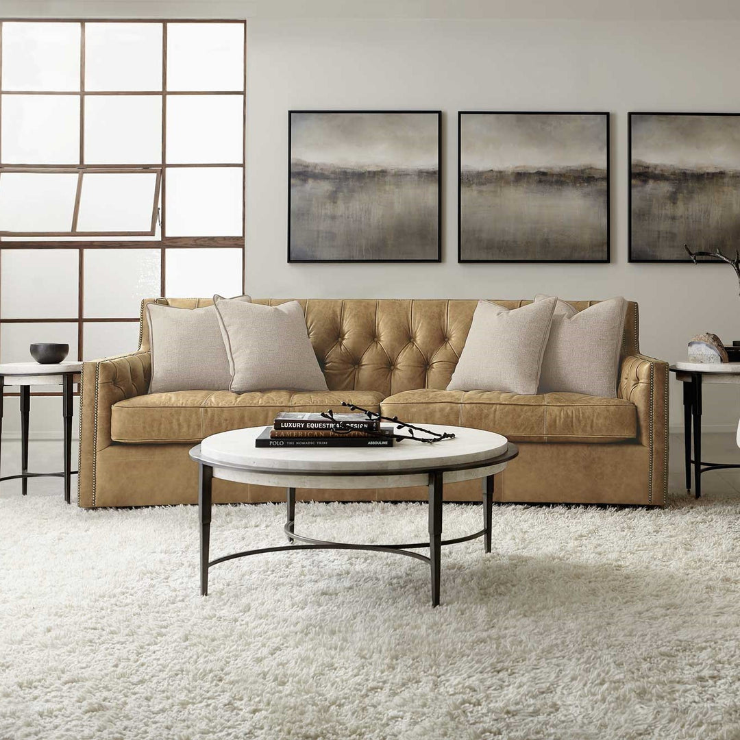 Tan leather sofa in living room with a metal and stone coffee table on top of a white shaggy rug.