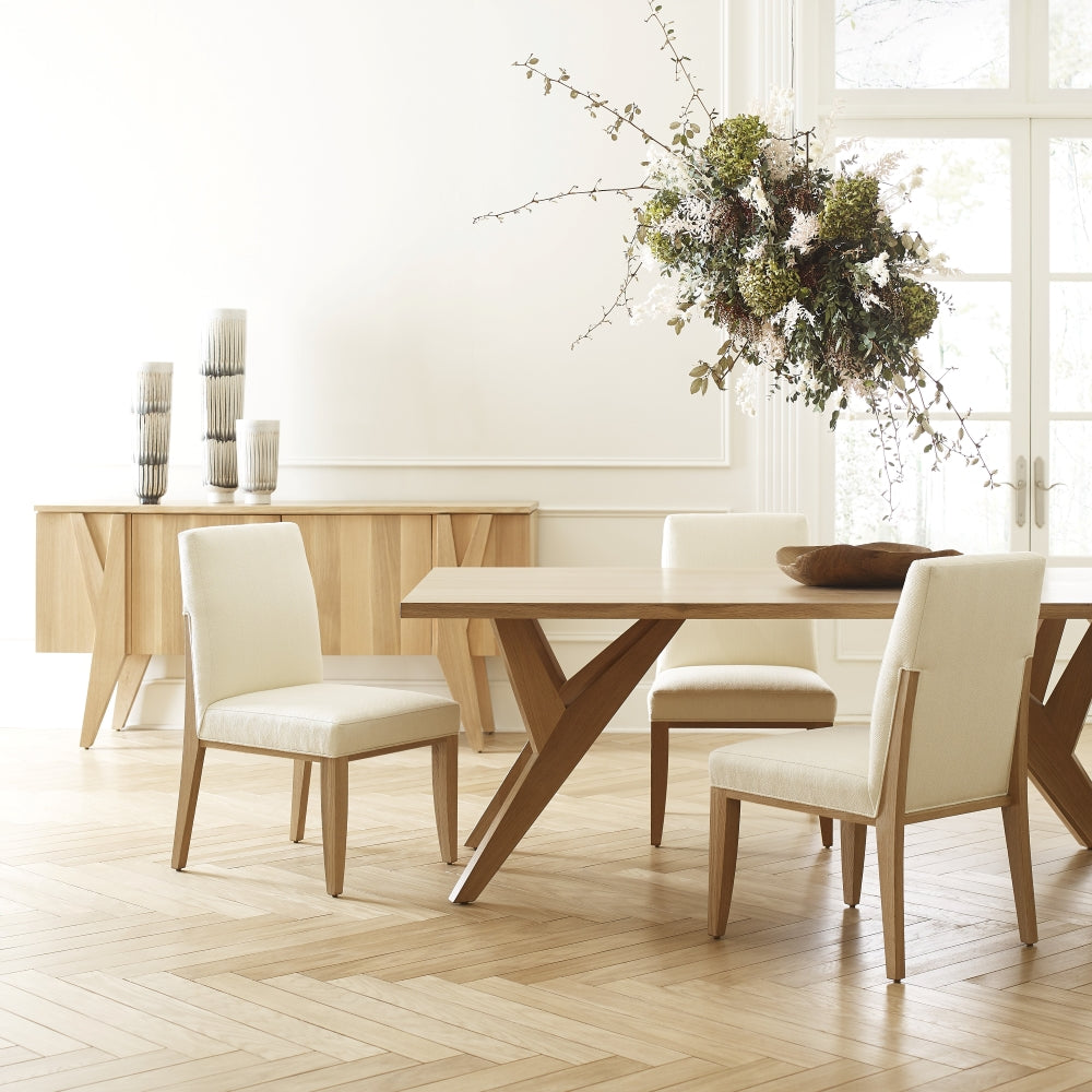 light wood dining table with white fabric chairs and a matching light wood credenza
