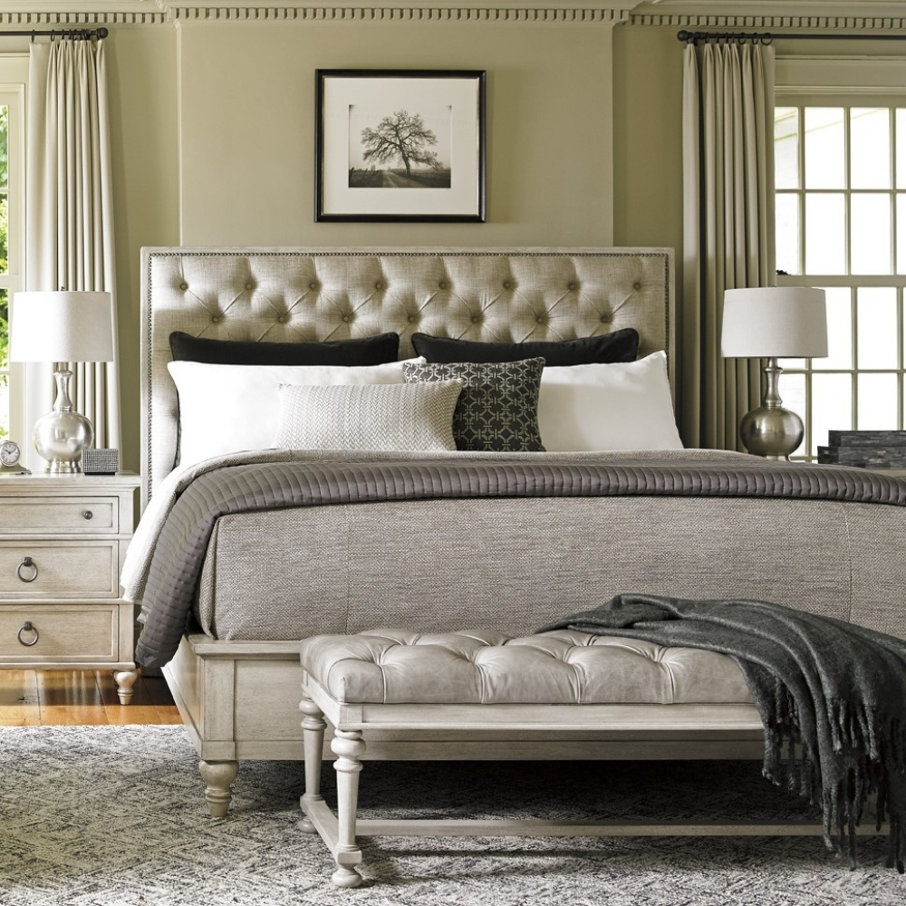 bedroom scene with large tufted bed, nightstand, and matching bench at foot of bed.