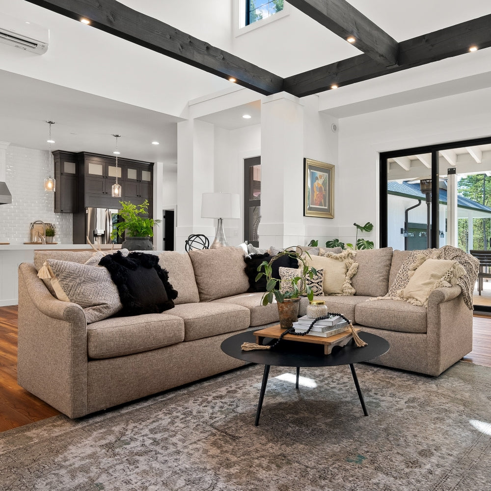 Light brown fabric sectional sofa with throw pillows and a round black coffee table in a large open living room.