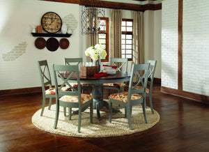Round cottage style dining table with dark wood top and painted green base surrounded by matching painted green wood dining chairs.