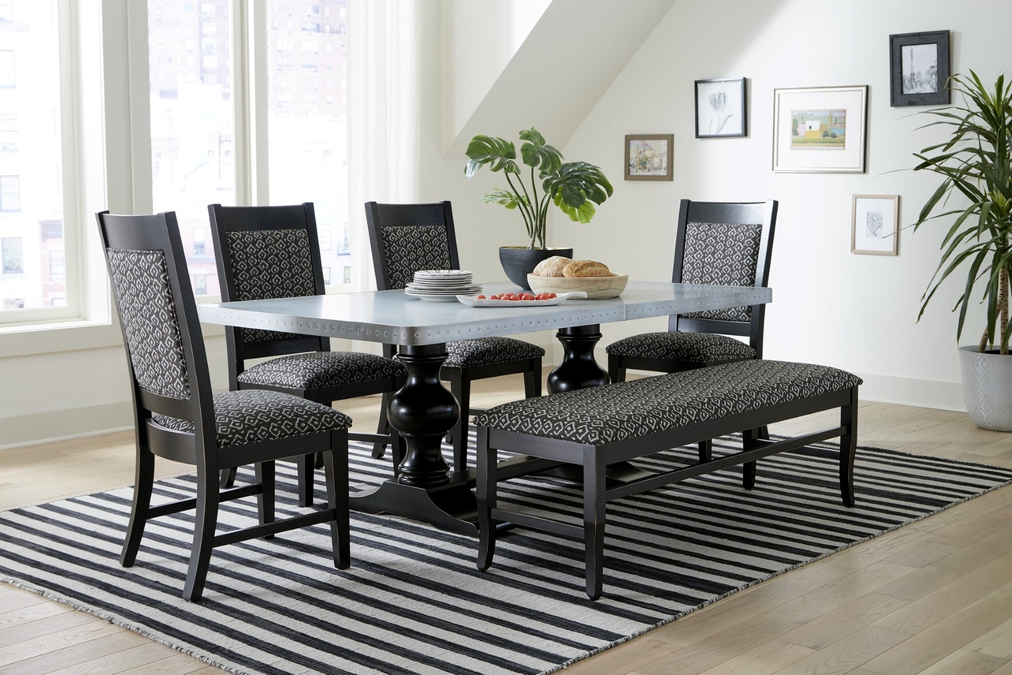 Dining table with zinc top surrounded by black dining chairs and matching bench