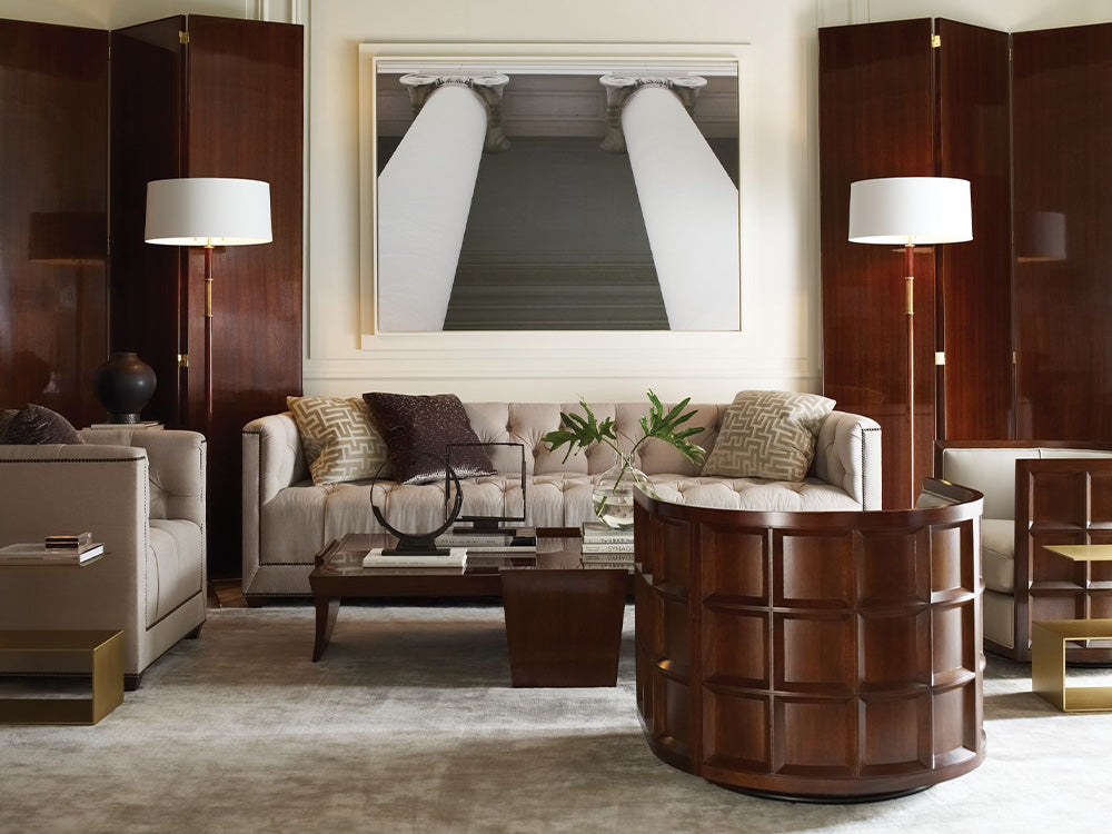 A modern living room scene from Baker furniture featuring a tufted sofa and a dark wood tub chair.