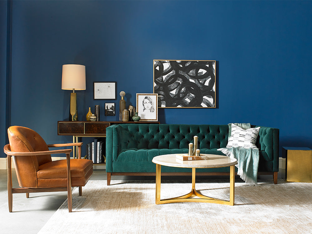 A modern living room scene from Precedent furniture featuring a teal tufted sofa and a tan leather and wood chair.