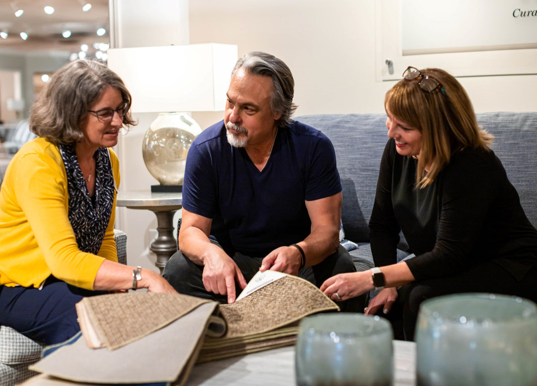 An interior designer discusses fabric samples with two customers sitting on a sofa.
