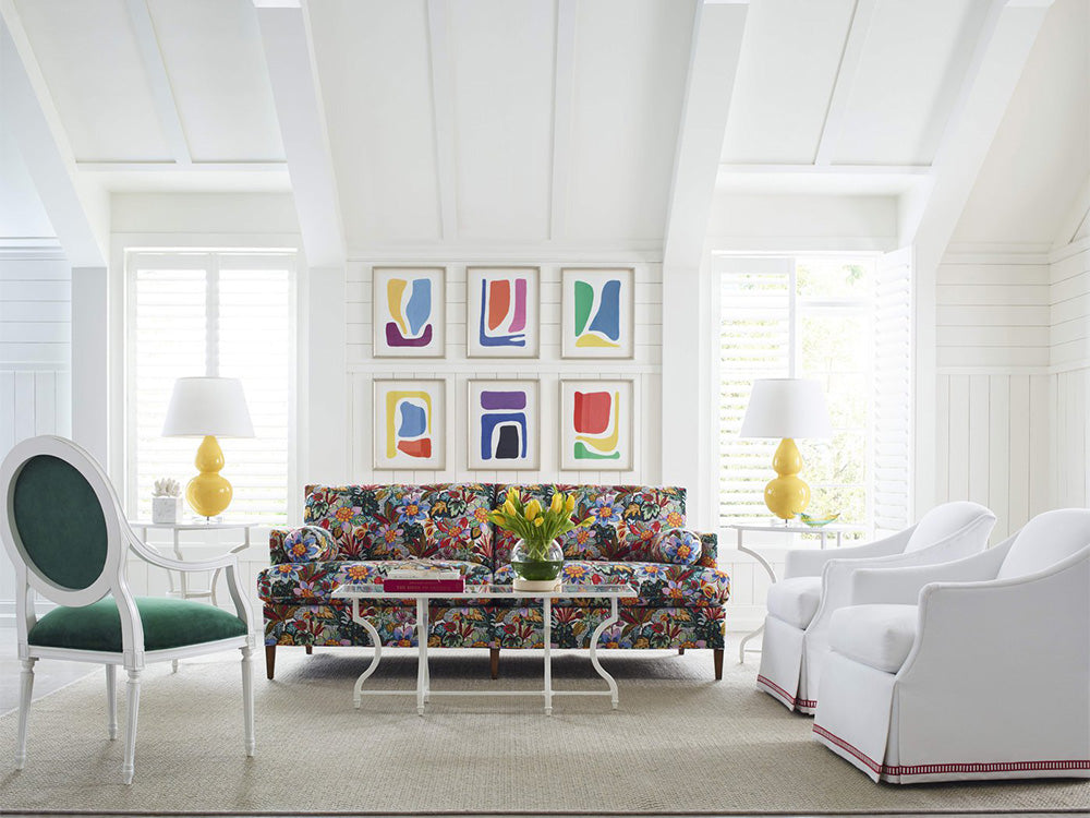 A living room scene from Taylor King featuring a sofa upholstered in a brightly colored floral fabric with two white fabric chairs.