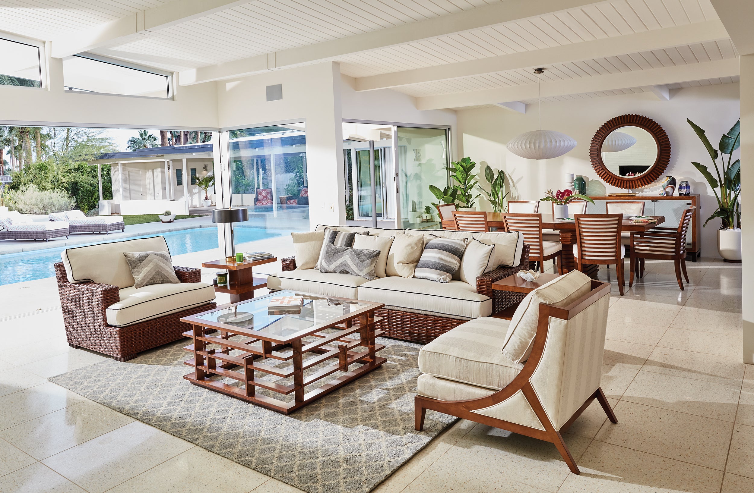 A living room scene from Tommy Bahama Home's Island Fusion collection featuring a rattan and fabric sofa and arm chair with a wood and glass modern cocktail table.