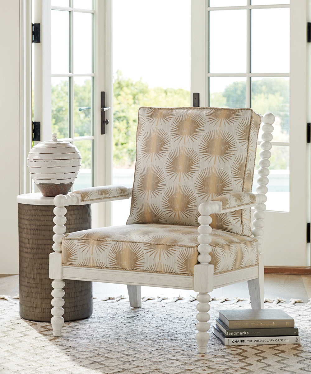A white arm chair with cushions upholstered in a beige geometric fabric.