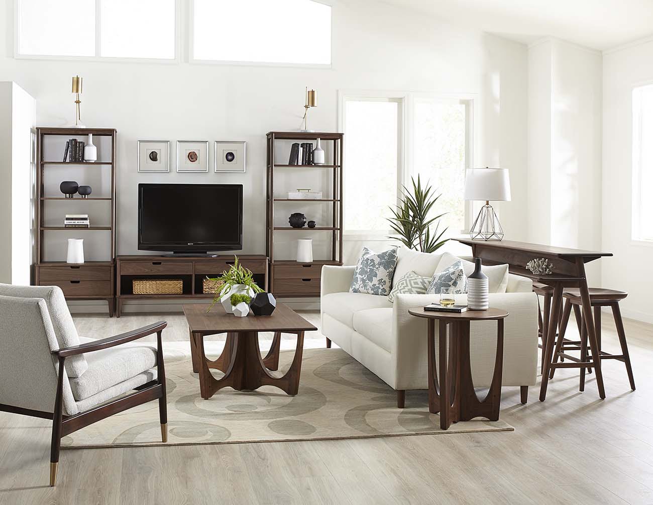 Living room scene featuring Stickley's Walnut Grove collection with a white sofa and chair, wood entertainment center, wood coffee and side tables, and a wood gathering table with stools.