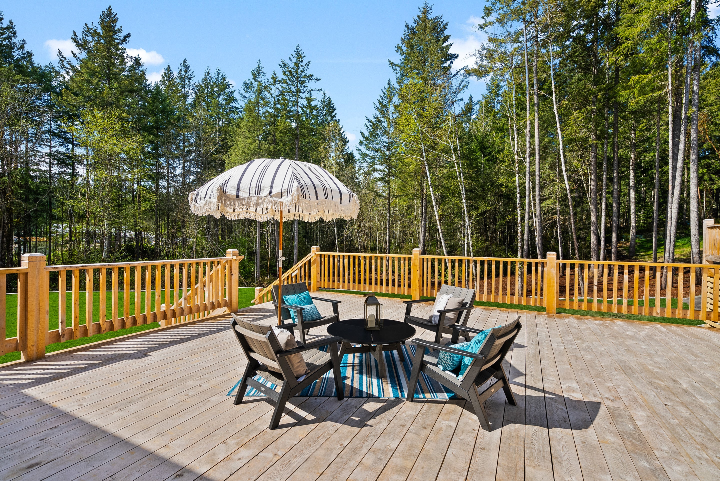 Four low sitting chairs with an umbrella around a small coffee table on a large outdoor deck.