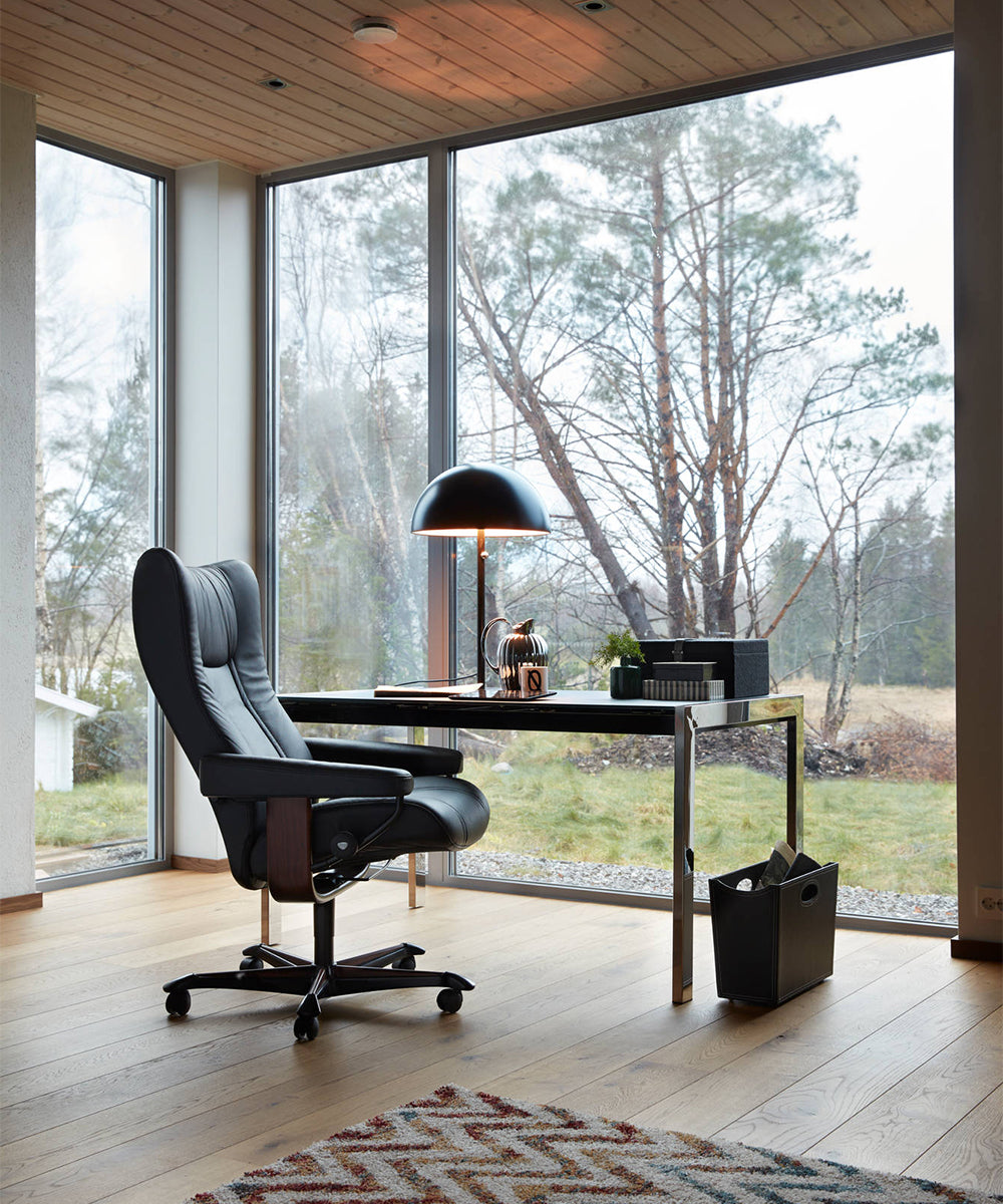 A black leather desk chair with wheels in front of a simple metal desk.