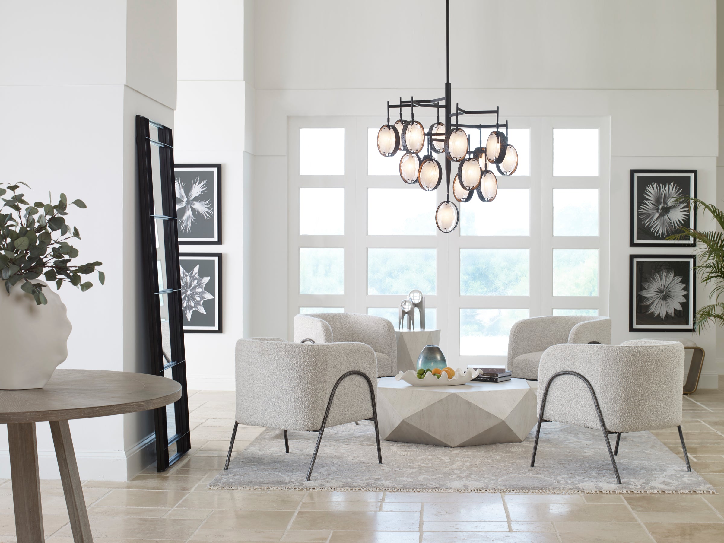 four white arm chairs sit around a geometric white coffee table underneath a metal and glass chandelier.